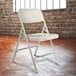 A white National Public Seating metal folding chair in front of a brick wall.