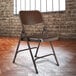 A brown National Public Seating metal folding chair in front of a brick wall.