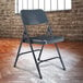 A National Public Seating metal folding chair in front of a brick wall.