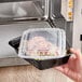 A hand holding a Choice black rectangular plastic microwavable container filled with food.