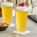 Two Acopa mixing glasses of beer on a table with a bowl of nuts.