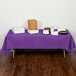 A table with a Creative Converting Amethyst Purple tablecloth and food on it.