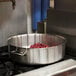 A large silver Vollrath brazier pot with red meat cooking inside on a stove.