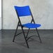 A black metal National Public Seating folding chair with blue plastic back and seat.