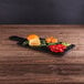 An Elite Global Solutions faux slate serving board with a plate of oranges, peppers, and other vegetables on a wood table.