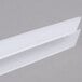 White plastic Fineline Tiny Temptations tongs on a gray surface.