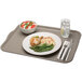 A rectangular gray Cambro cafeteria tray with food including a bowl of tomato and cheese salad, a glass of water with ice and lemon, and a white napkin with a fork and knife.