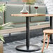 A FLAT Tech round black cast iron table base with two tables and chairs, one with a glass and a wine glass on it.