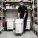 A man in black pants and a black shirt pushing a large white Cambro ingredient storage bin with a sliding white lid.