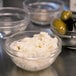 A close-up of a clear glass bowl filled with cheese and olives.