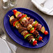 A Tuxton cobalt oval china platter with skewered meat and vegetables on a table.