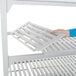 A person's hand holding a white Cambro Camshelving® Premium vented shelf.