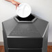 A hand putting a white plate into a black hexagonal trash can.