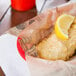 American Metalcraft newspaper deli wrap with a fried fish fillet and a lemon wedge.