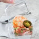 A person holding a clear plastic container with shrimp, jalapenos, and salsa.