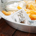 A bowl of french fries with newspaper deli paper on a table.