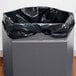 A black plastic bag in a grey hexagonal Commercial Zone trash container with an open top.