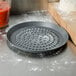 An American Metalcraft Super Perforated Hard Coat Anodized Aluminum Pizza Pan on a counter with flour.