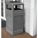 A grey rectangular Commercial Zone waste container with an ashtray dome lid on a porch.
