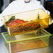 A person in a white coat holding a large piece of meat in a clear plastic colander pan.