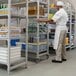 A man in a white coat and hat standing next to a Cambro Camshelving® track extension shelf.