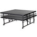 A National Public Seating Transfix portable stage with gray carpet on a black rectangular table.