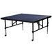 A National Public Seating Transfix stage with blue carpet on a rectangular table with wheels.