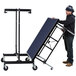 A man pushing a National Public Seating Transfix portable stage with blue carpet on a dolly.