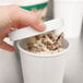 A hand holding a white Choice paper lid over a bowl of frozen yogurt.