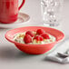 A Tuxton Cinnebar grapefruit bowl filled with fruit and nuts on a table.