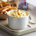 A tray with a Choice white paper food cup filled with macaroni and cheese and fries on a school kitchen counter.