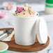 A white paper double-wall frozen yogurt or food cup with a matching paper lid, filled with swirled dessert and colorful toppings.