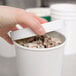 A hand holding a white container with a white plastic lid over ice cream.