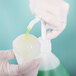 A person in white gloves pouring green Carnival King Lime Snow Cone Syrup into a cup.