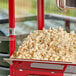 A red Carnival King popcorn machine filled with popcorn in a container.