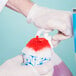 A person using a dispenser to add red Carnival King fruit punch syrup to a bowl of shaved ice.