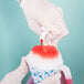 A person in white gloves pouring red Carnival King Watermelon Snow Cone Syrup into a cup of snow.