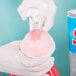 A person in white gloves pouring red liquid from a blue bucket into a bowl of snow.