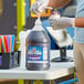 A woman in gloves pouring Carnival King Grape Snow Cone Syrup into a large container.