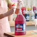 A large gallon jug of Carnival King watermelon snow cone syrup with a pump dispenser being used to flavor a snow cone.