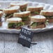 A plate of sandwiches on a table with American Metalcraft mini chalk cards in front of each sandwich.