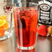 A Libbey mixing glass filled with red liquid, ice, and orange slices.