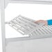 A person installing a white Cambro Camshelving unit with vented and solid shelves.