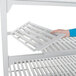 A hand holding a white Cambro Camshelving Premium vented shelf.