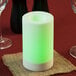 A white Sterno flameless candle with a green and white color changing flame on a table with wine glasses and a burlap napkin.