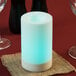 A white Sterno flameless pillar candle with a blue light on a table with a red and black tablecloth.