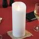 A white Sterno Mirage flameless LED candle flickering on a table with wine glasses.