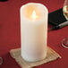 A Sterno Mirage cream LED candle on a table with a glass of wine.