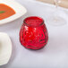 A red glass candle holder with a Sterno red wax candle on a table.