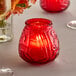 A red glass candle holder with a lit red candle inside.